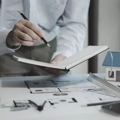 Architecte prenant des notes dans un carnet au dessus des plans de la maison